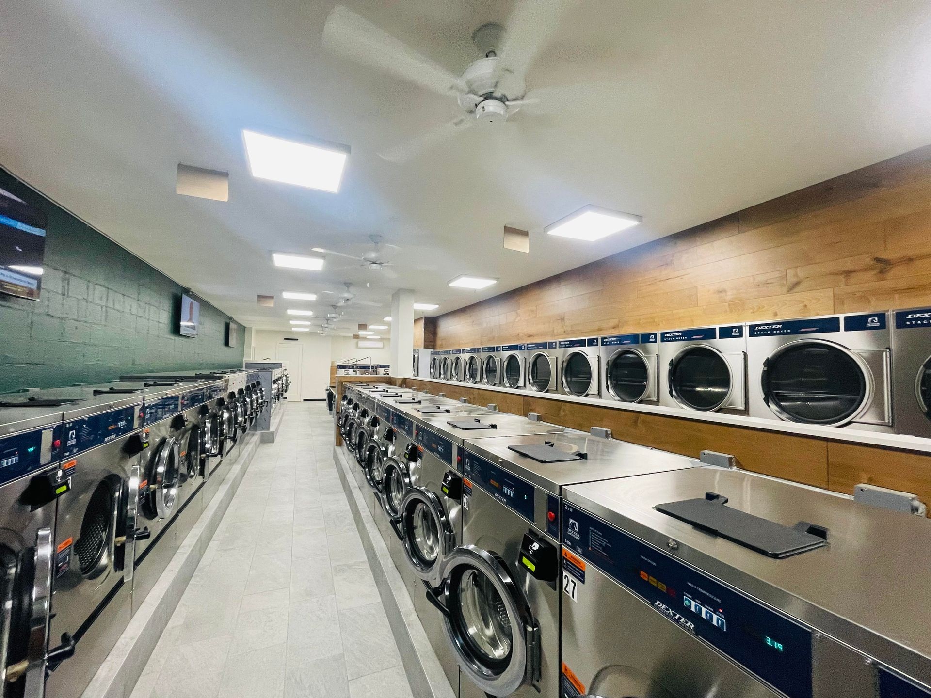 Modern laundromat interior with rows of washing machines and dryers under bright ceiling lights.