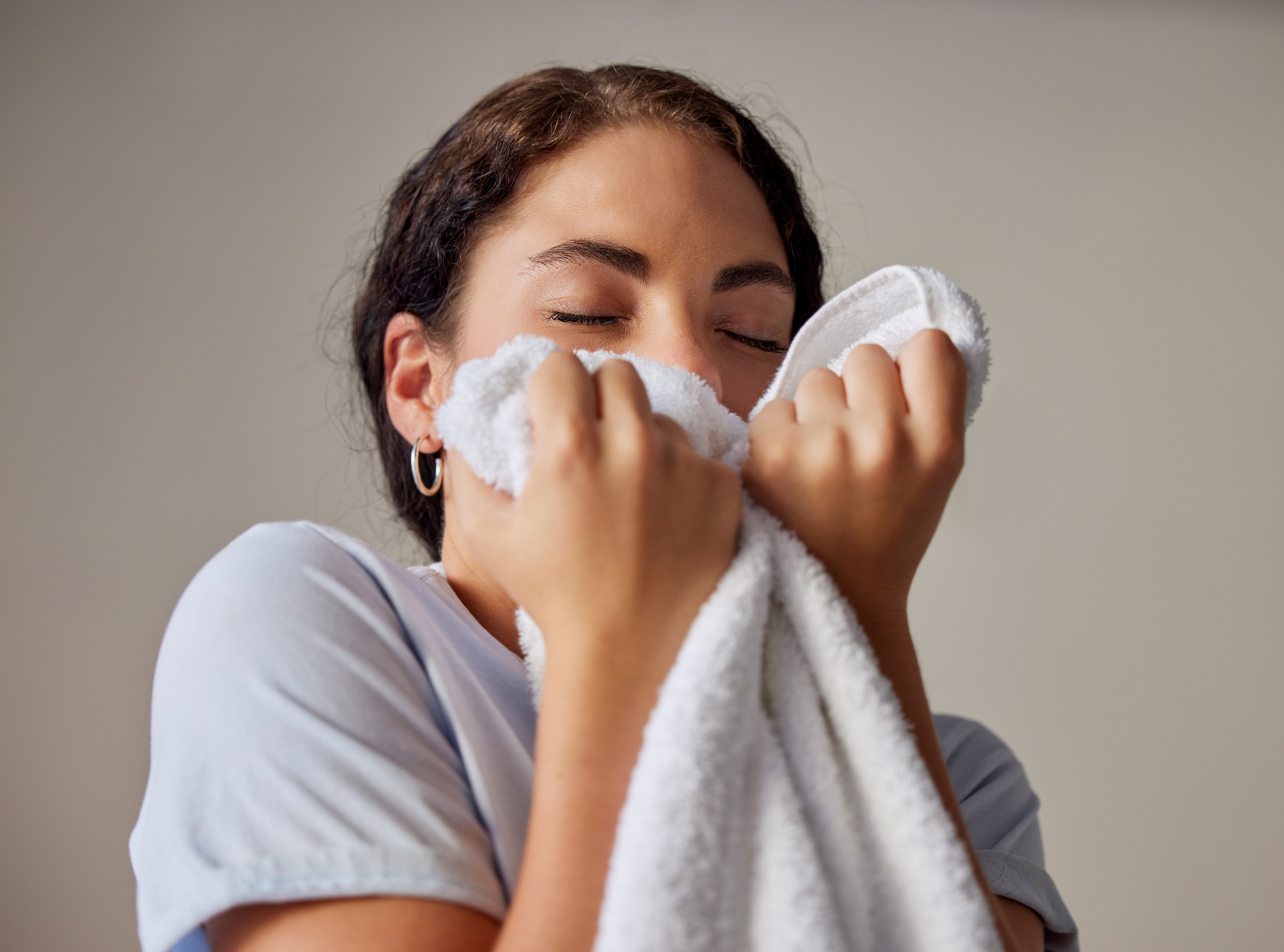 Woman smelling a clean towel after doing laundry at her home, hotel or resort while spring cleaning. Housekeeping, maid or housewife doing washing for maintenance, hygiene and fresh fabrics or cloth.